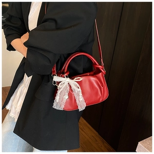 Detalle de bolso tipo cubo rojo plisado con lazo de encaje blanco y colgante perla