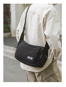 Close-up of black nylon messenger bag with woven brand label and adjustable strap