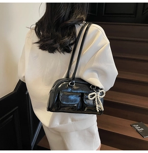 Detail of black glossy leather underarm bag with pearl bow charm and twin handles