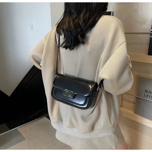 Detail of a black glossy crossbody bag featuring a silver metal abstract logo on the flap