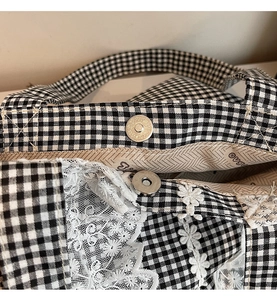Detailed view of black and white plaid tote bag with floral lace trim and magnetic buckle