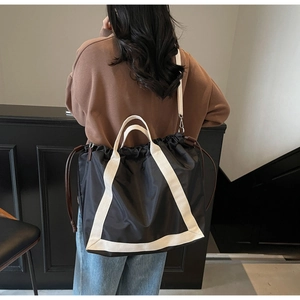Detail of black nylon tote bag featuring white canvas straps and drawstring closure design