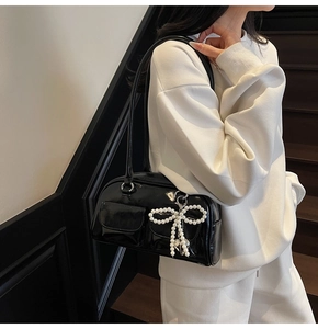 Detail of black glossy underarm bag with decorative pearl bow and textured front pocket