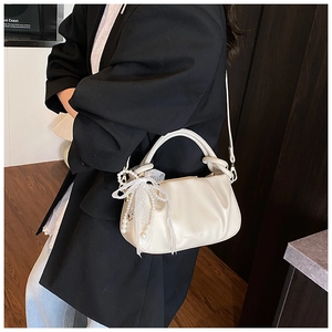 Detalle de bolso de hombro plisado crema con colgante de perlas y encaje