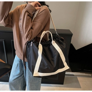 Detail of black drawstring tote bag with off-white handles and wide canvas shoulder strap