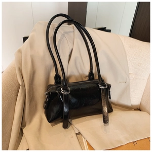 Close-up of black glossy pillow bag with silver buckles on beige textured fabric