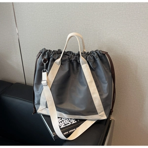 Detail of grey drawstring tote bag with contrast cream canvas straps on a leather sofa