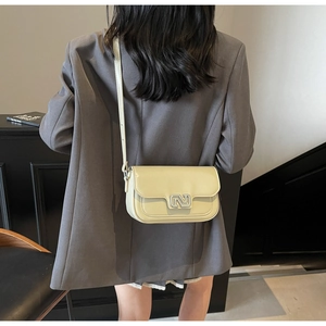 Close-up of cream crossbody bag featuring a minimalist N-shaped buckle on dark blazer
