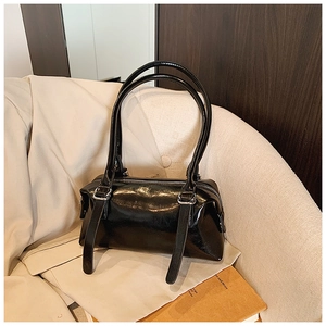 Detail of glossy black leather shoulder bag with silver hardware on a cream blazer