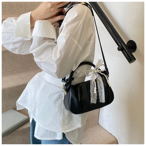 Detalle de bolso tipo cubo en cuero negro con lazo de encaje blanco y cadena de perlas