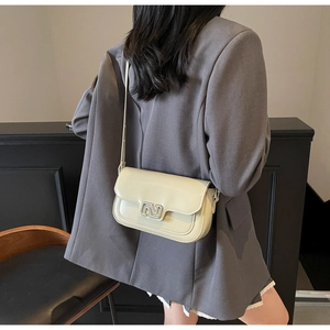 Detail of a creamy white glossy leather crossbody bag with a silver N-shaped buckle