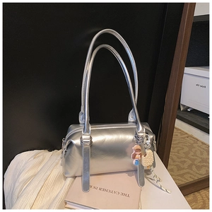 Detail of silver mirror Boston bag featuring metal handles and cute cartoon doll charms
