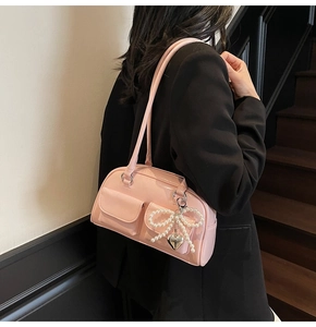 Detail of pink patent leather underarm bag with pearl bow charm on black blazer
