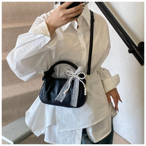 Detalle del bolso tipo saco negro plisado con lazo de encaje blanco y cadena de perlas