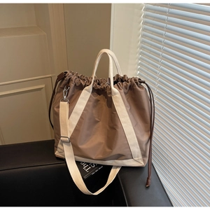 Detail of a brown nylon tote bag with drawstring closure and cream-colored canvas straps