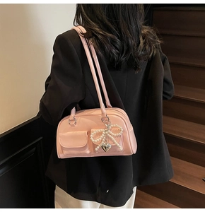 Detail of pink patent leather shoulder bag with decorative pearl bow and metal heart charm