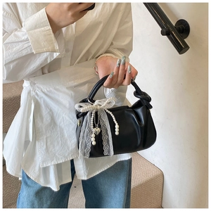 Detalle del bolso de cubo plisado negro con lazo de encaje blanco y perlas