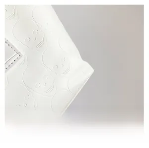 Macro shot of white leather texture featuring 3D embossed skull patterns on a tote bag