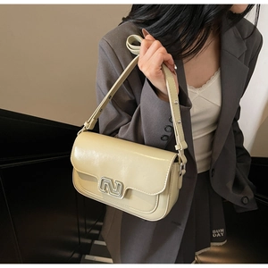 Close-up of cream crossbody bag featuring a modern silver N-shaped metal buckle detail