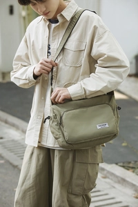 Detailed close-up of olive green nylon dumpling bag with adjustable strap and brand label