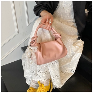 Detalle del bolso de cubo rosa plisado con asa anudada y colgante de lazo y perla