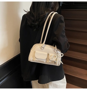 Detail of off-white leather underarm bag with pearl bow pendant worn by a model