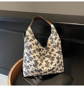 Detalle del bolso tote de lona con estampado de vaca y asas de cuero marrón en silla