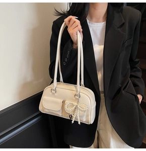 Detail shot of a minimalist cream white underarm bag with a pearl bow charm on a model