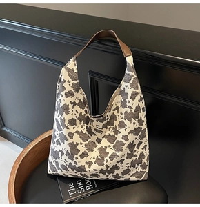 Detalle del bolso hobo con estampado de vaca y asas de cuero marrón en silla de madera