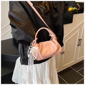 Detalle de bolso tipo cubo rosa plisado con colgante de perlas y correa de hombro