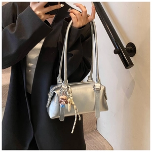 Close-up of silver pillow bag with metallic finish and cute doll charm on strap