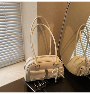 Detail of a creamy white glossy leather shoulder bag with pearl bow heart pendant and twin straps