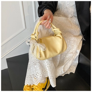 Detalle del bolso tipo saco amarillo claro con lazo de encaje y perlas y asa anudada