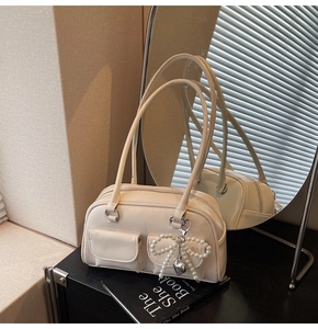 Detail of cream shoulder bag featuring double front pockets and a pearl bow charm