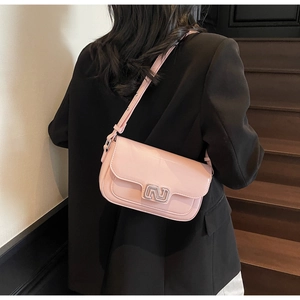 Shoulder shot of a light pink flap handbag with adjustable strap and silver metal buckle