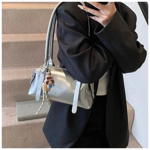 Metallic silver Boston handbag with a cartoon charm worn by a model in a black suit