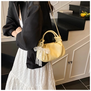 Detalle de bolso saco plisado amarillo con colgante de lazo de encaje y perlas