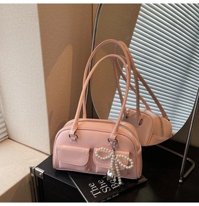 Close-up of pink leather handbag with pearl bow charm and dual front pockets