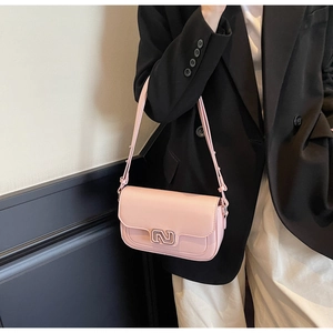 Close-up of pink leather crossbody bag with geometric metal buckle on black blazer