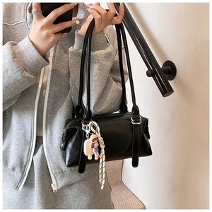 Detail of black glossy leather shoulder bag with cute doll charm and long straps