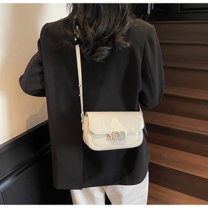 Detailed back view of a cream leather crossbody bag worn by a model in a black blazer