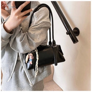 Detail of minimalist black faux leather pillow bag with cartoon and woven rope charms