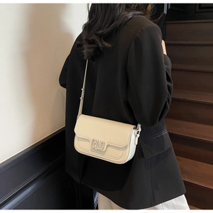Close-up of a cream leather crossbody bag with silver N-shaped clasp worn by a model