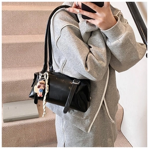 Detail of black patent leather cylinder bag with cute charm and long shoulder straps