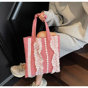 Detail of red gingham fabric tote bag featuring intricate white lace trim and cloth handles