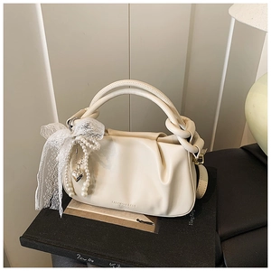 Detalle de bolso saco plisado crema con asa anudada y colgantes de perlas y corazón