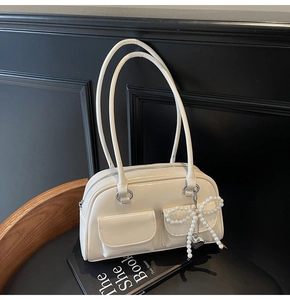 Detail of cream glossy leather handbag with pearl bow and silver heart charm