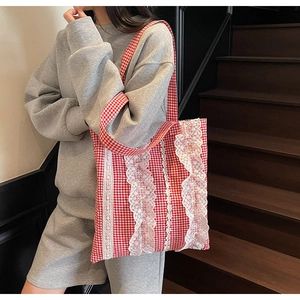 Detail of red gingham tote bag featuring intricate white lace trim and plaid shoulder straps