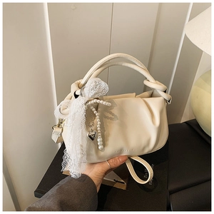 Detalle de bolso tipo cubo plisado crema con pañuelo de encaje, perlas y colgante de corazón