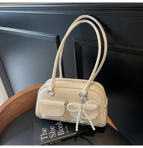 Detail view of cream Boston shoulder bag featuring a pearl bow pendant and dual pockets